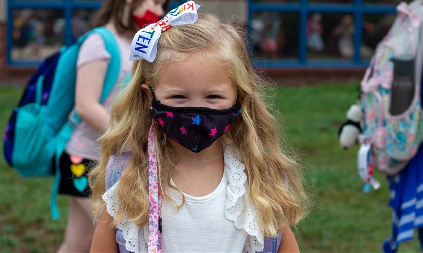 A girl wearing white smiles while wearing a mask
